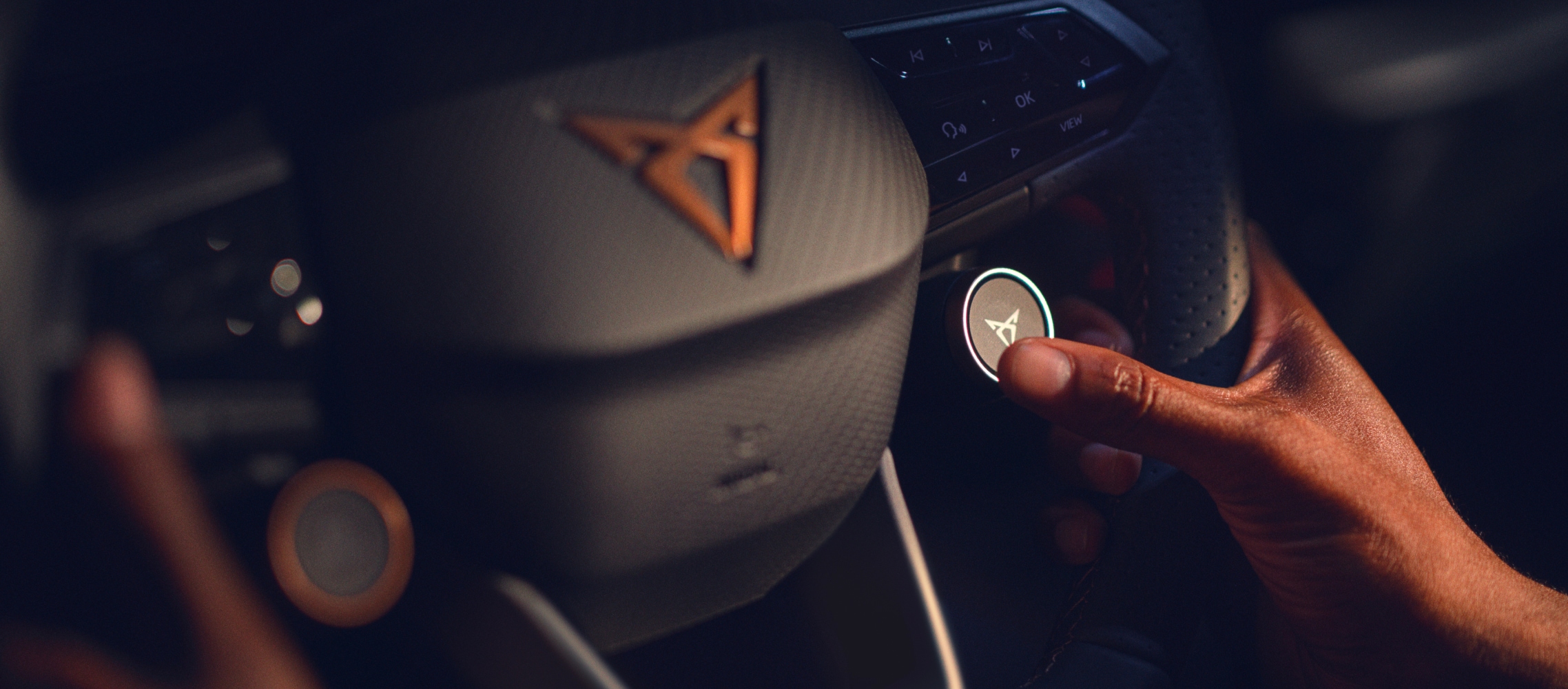 Cupra born steering wheel with satellite buttons and copper accent cupra logo, close up inside company car.